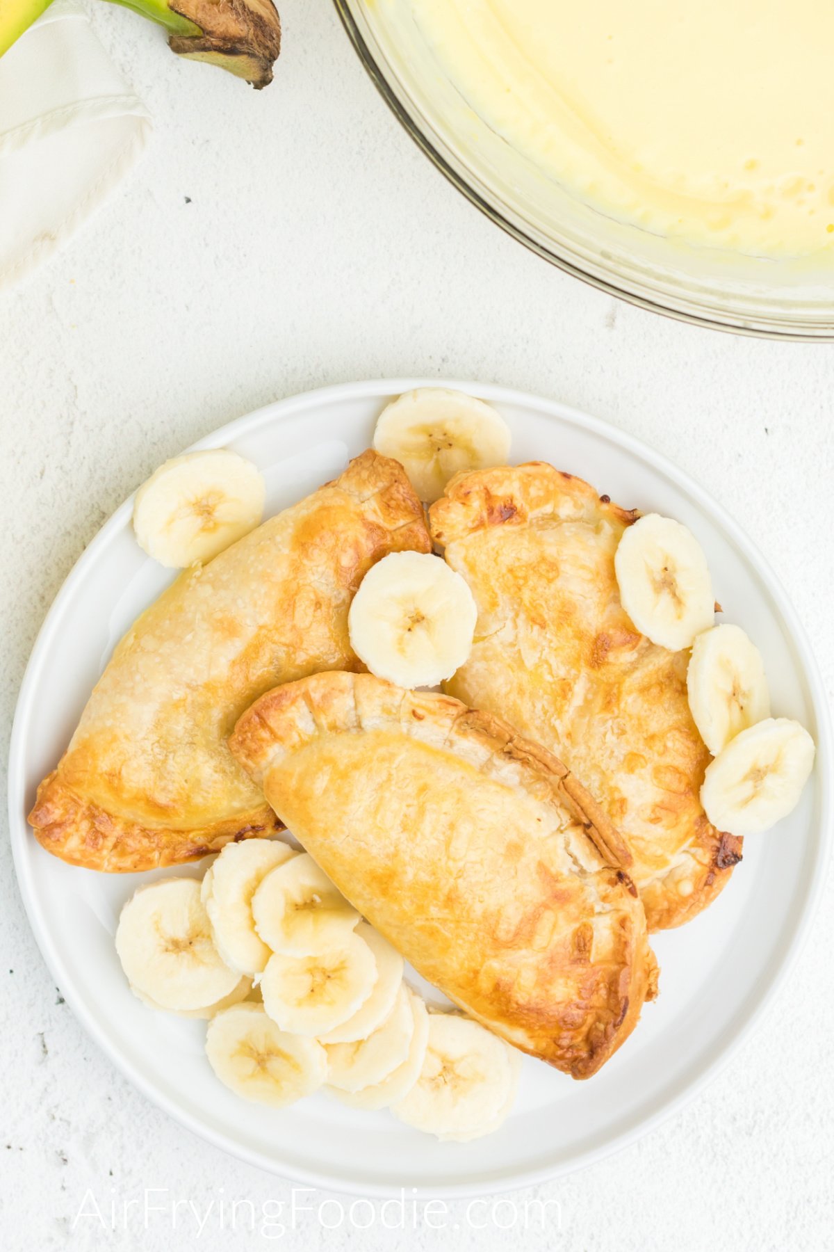 Air fried banana pudding pied on a plate with additional sliced bananas.