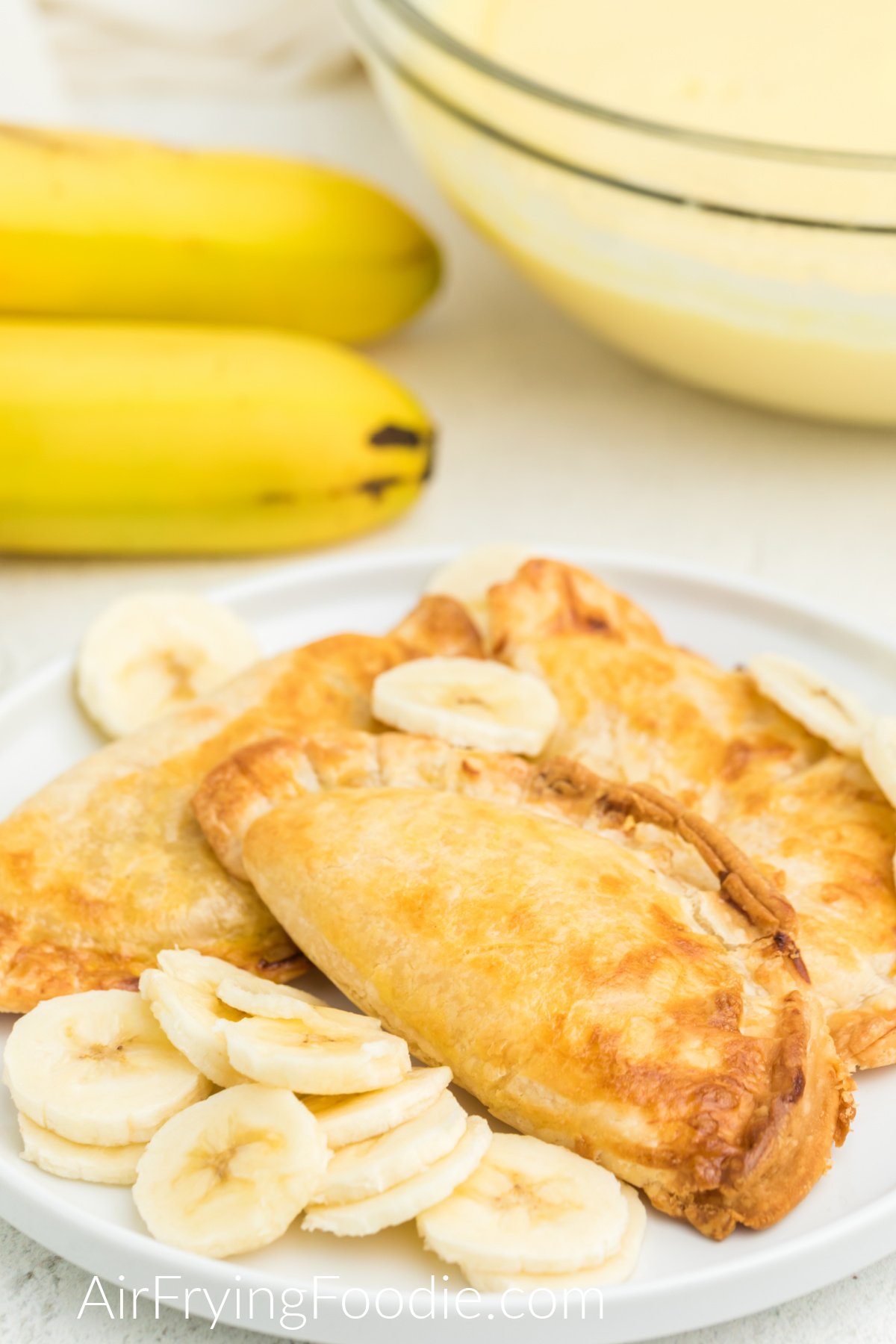 Banana Pudding Pies fried in the air fryer and served on a white plate with sliced bananas.