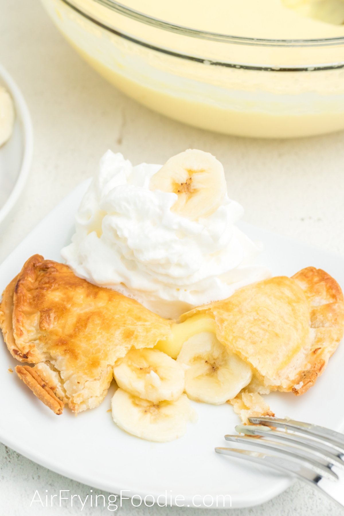 Banana Pudding Pie made in the air fryer on a white plate, with a side of whipped cream and a banana slice on top. 