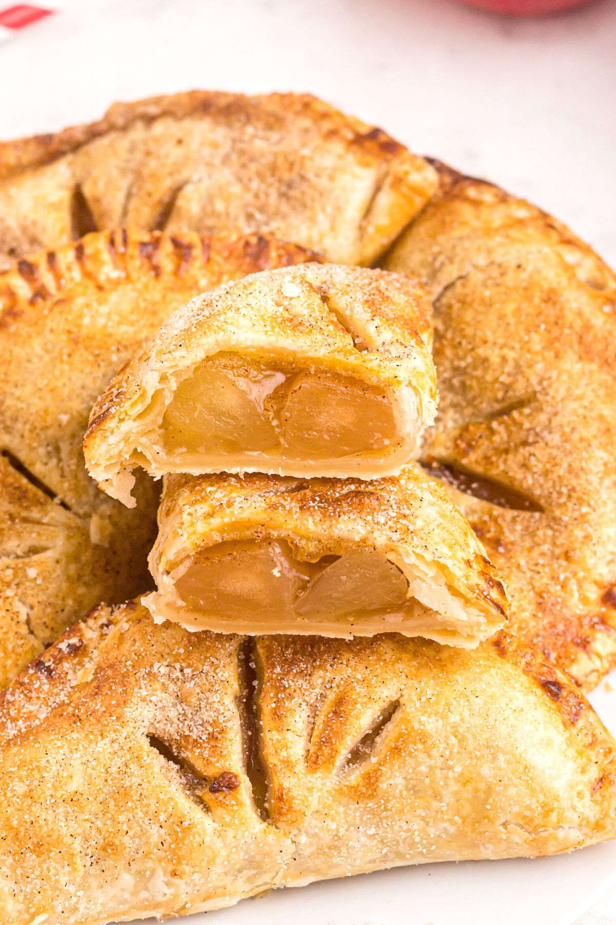 Crispy Air Fryer Apple Hand Pies 9 Stacked golden apple hand pies on a white plate, with one pie cut in half to reveal its gooey apple filling.