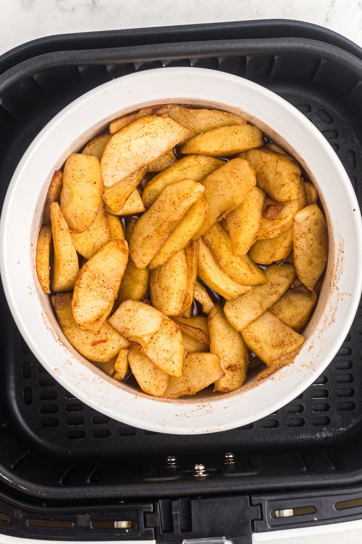 Golden juicy apple slices in a white bowl in the air fryer basket after being cooked