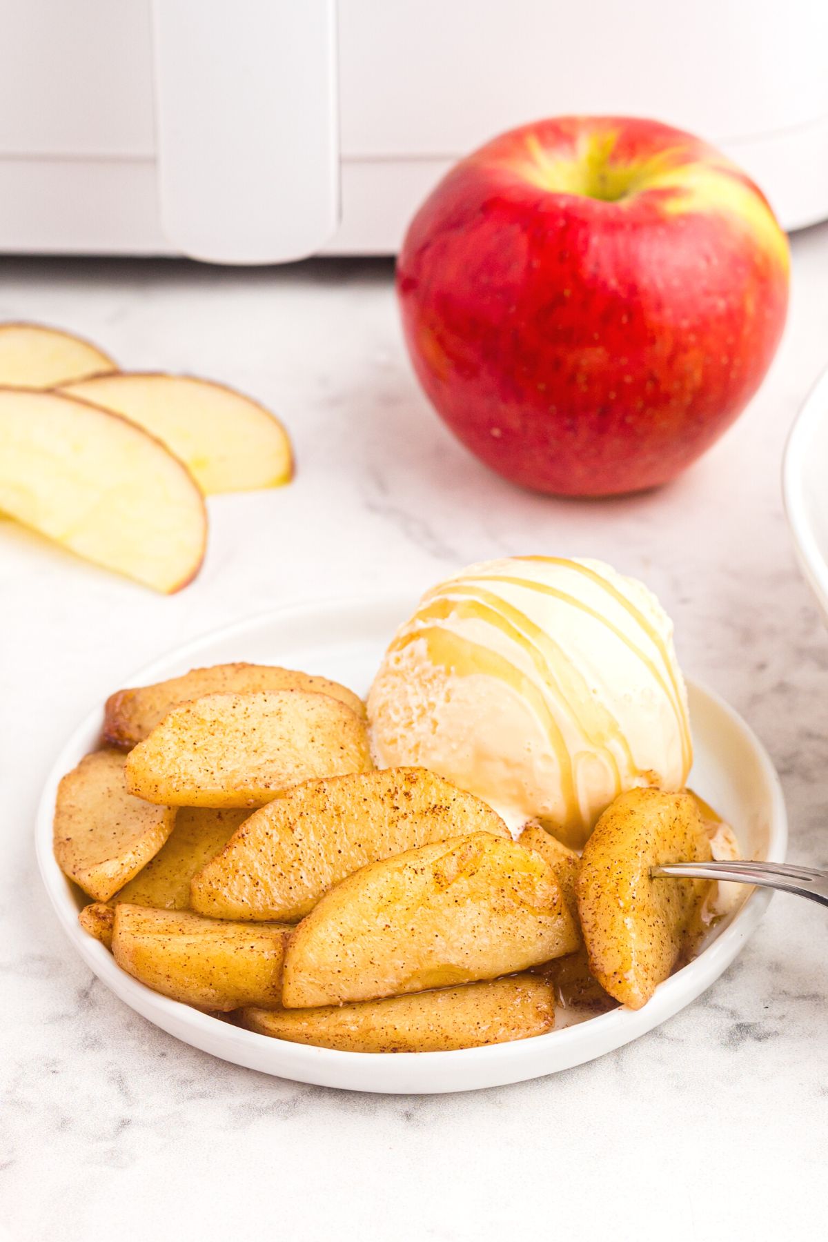 Sliced apples cooked in the air fryer on a plate with a scoop of ice cream.