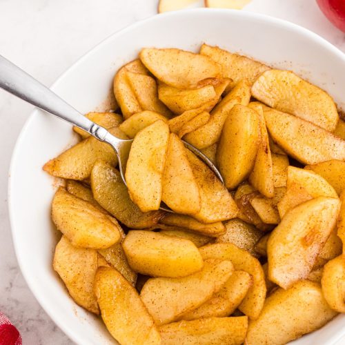 Golden juicy sliced apples in a white bowl being scooped with a spoon