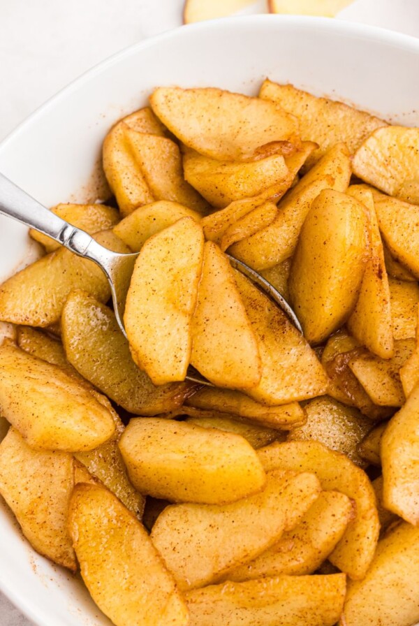 Golden juicy sliced apples in a white bowl being scooped with a spoon