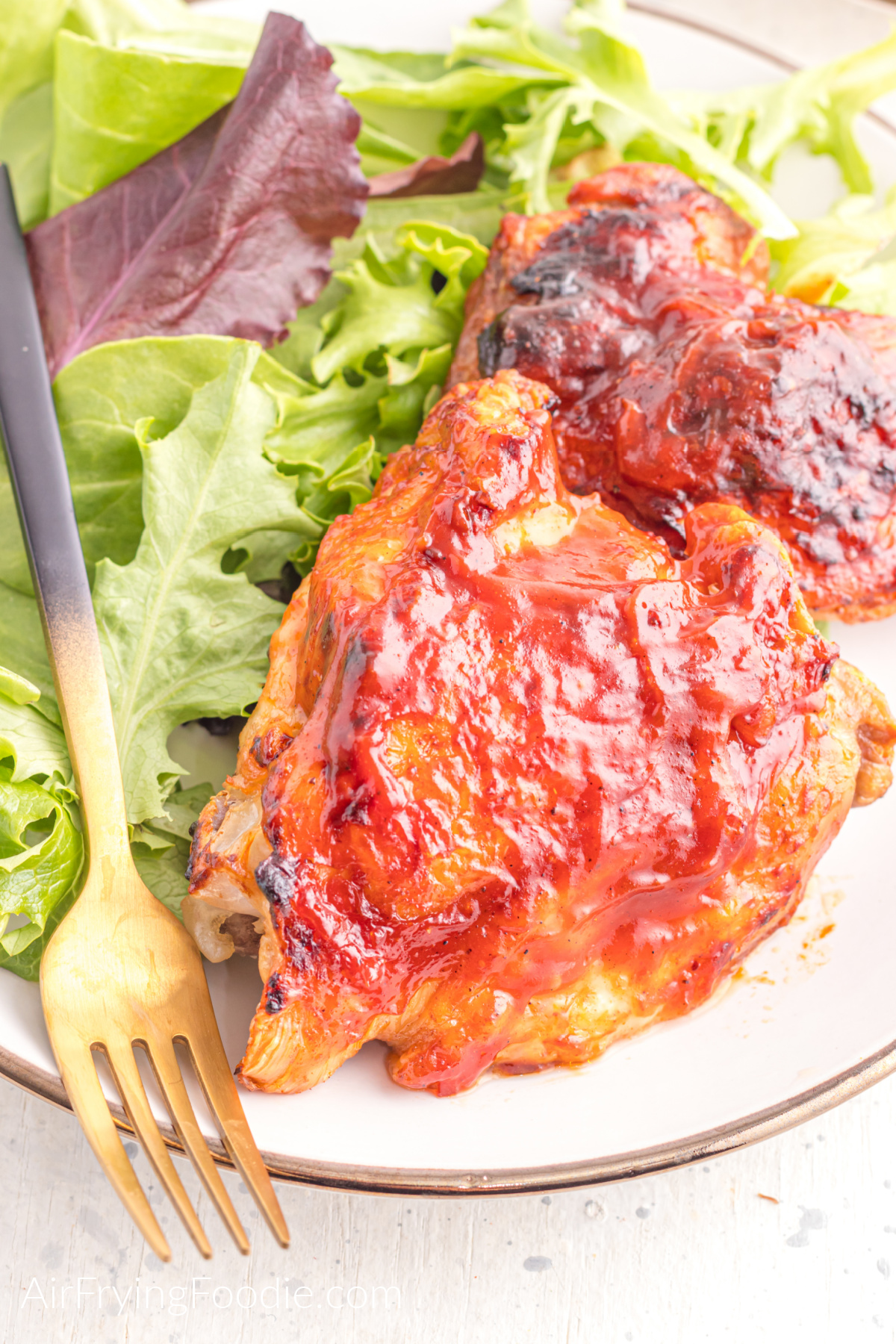 Air fried bbq chicken thighs on a plate with salad and a fork.