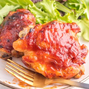 BBQ chicken thighs made in the air fryer on a plate with a fork and a salad.