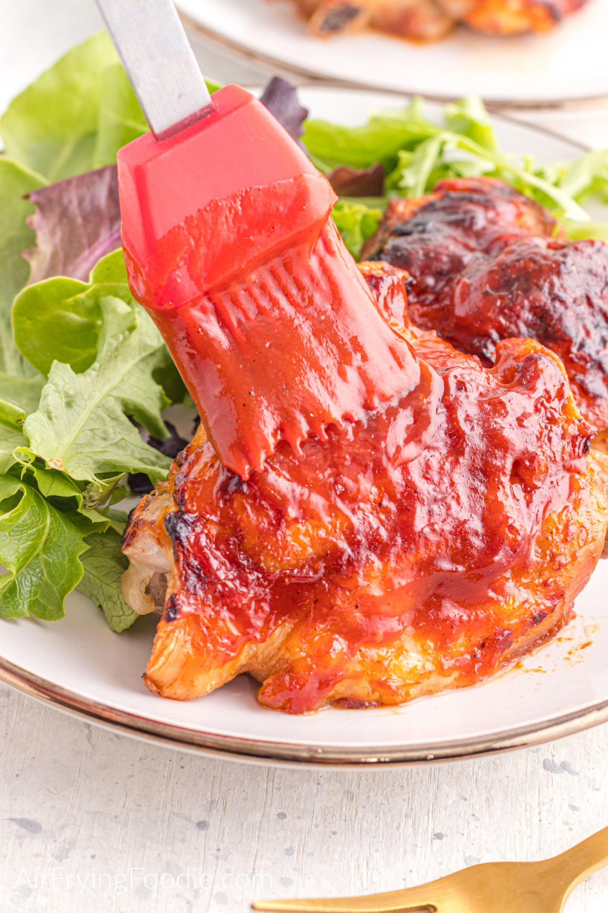 BBQ chicken thighs being brushed with additional BBQ sauce on a plate with a side salad.