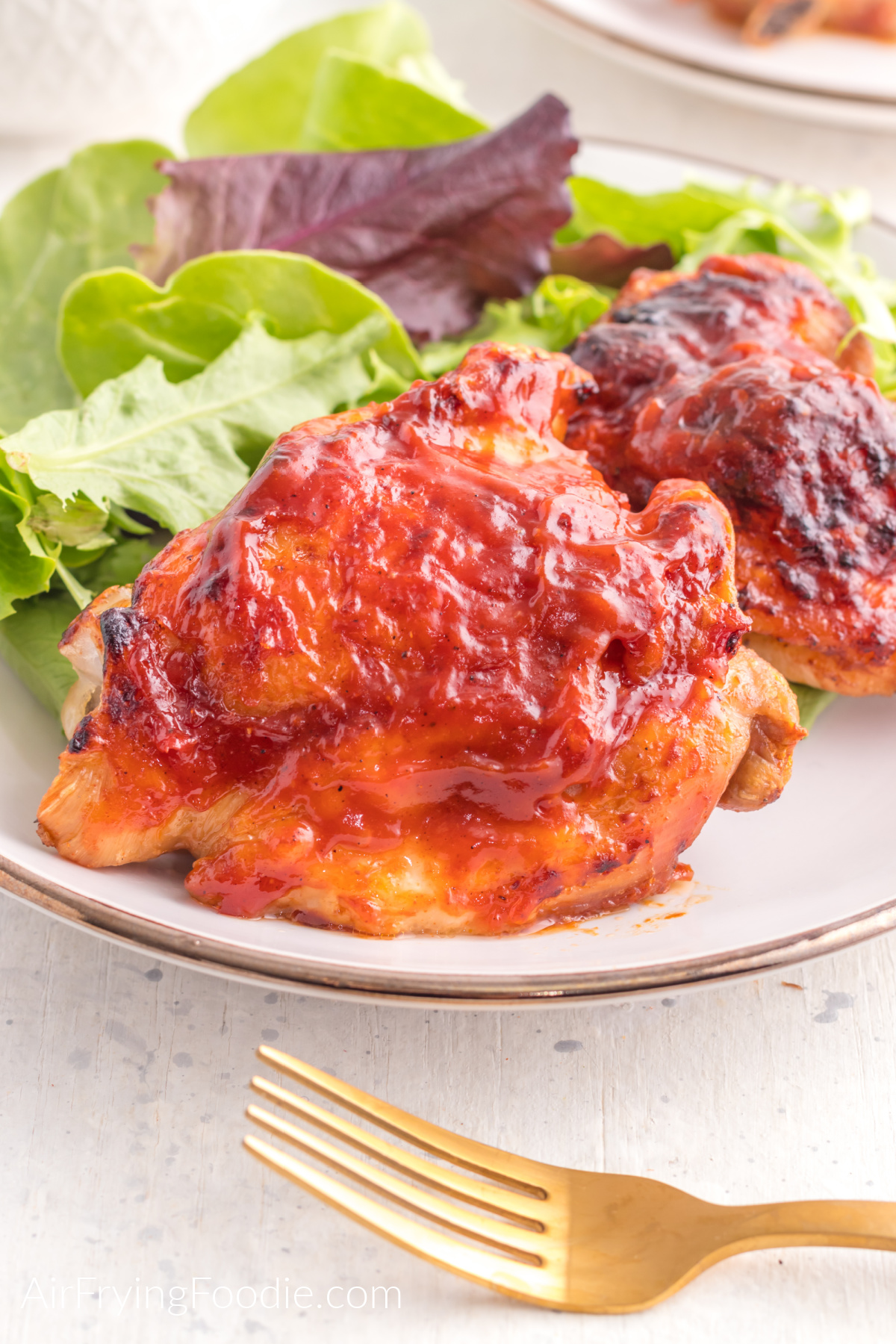BBQ chicken made in the air fryer on a plate with a side of salad. 