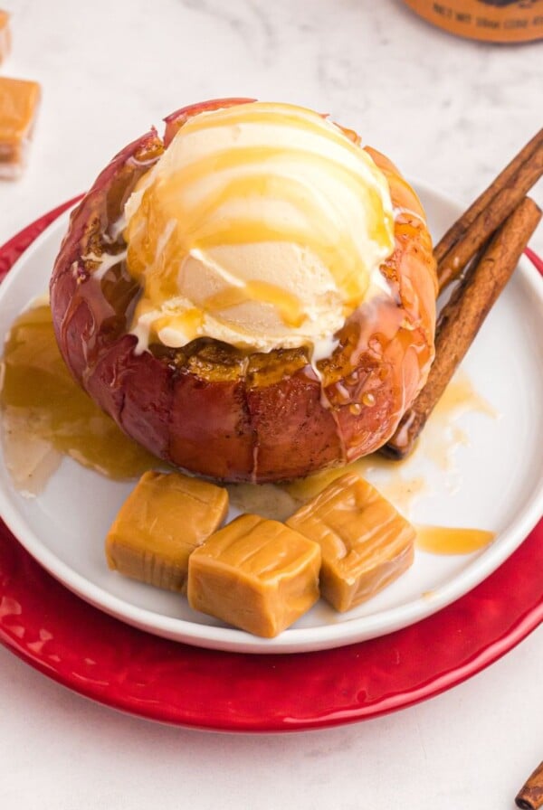 Ice cream on top of apple with caramel squares on a white plate