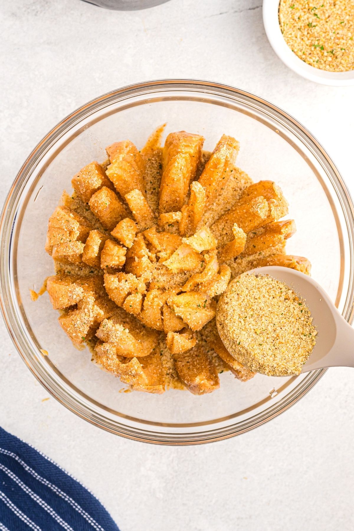 Spoon spreading breadcrumbs over battered onion in a glass bowl