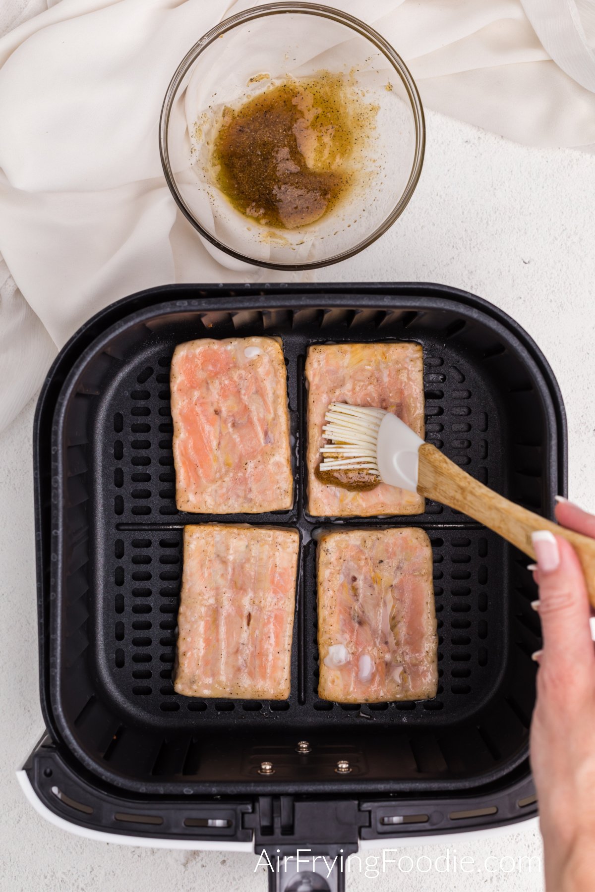 Frozen salmon in air fryer basket being brushed with marinade before finishing the cooking process.