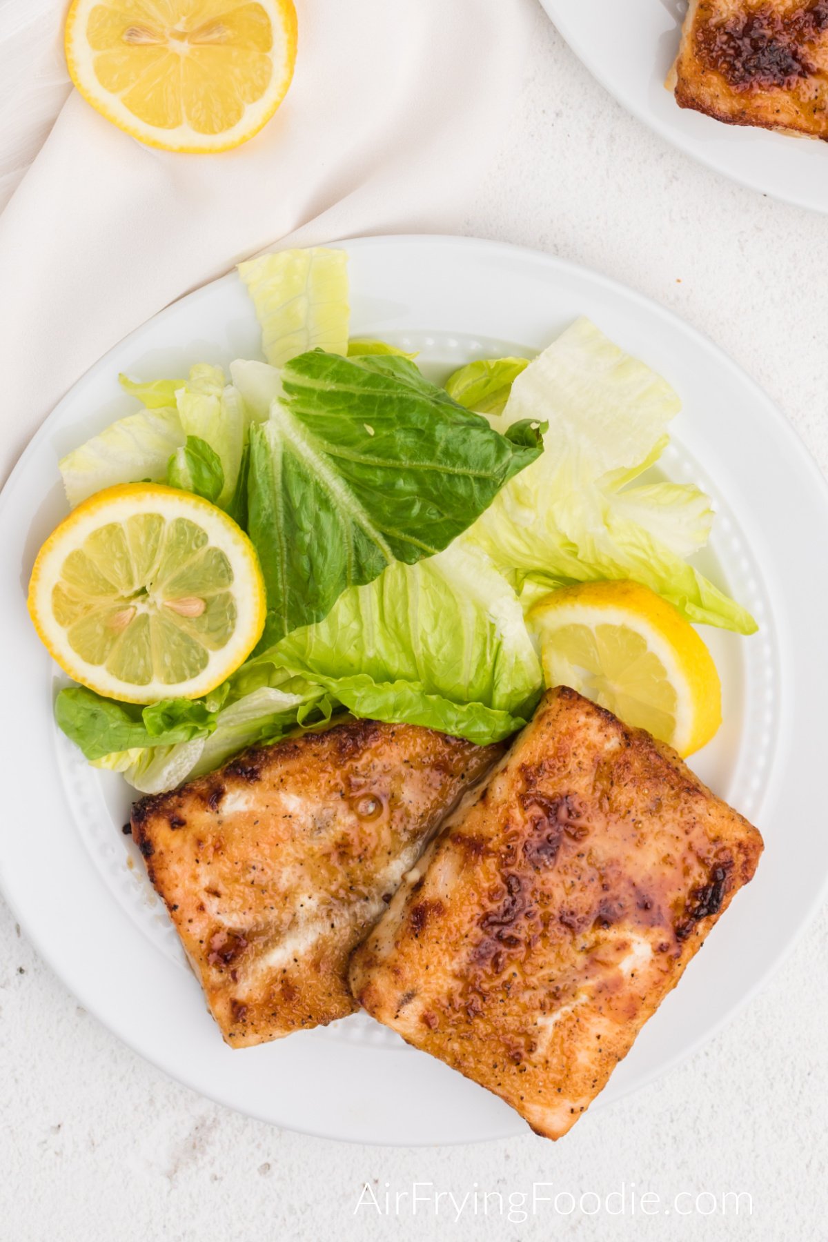Fully cooked Air fryer frozen salmon on a plate with salad and lemon slices. Ready to eat.