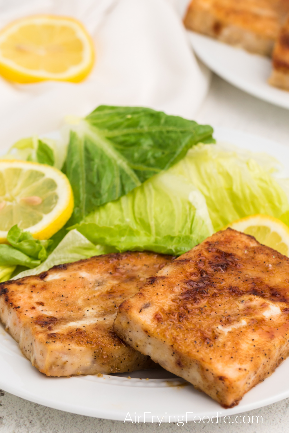 Seasoned salmon cooked from frozen in the air fryer, served on a white plate with a salad and lemon slices. 