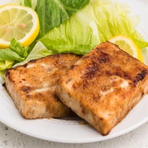 fully cooked air fryer frozen salmon on a white plate with a side salad and a lemon slice.