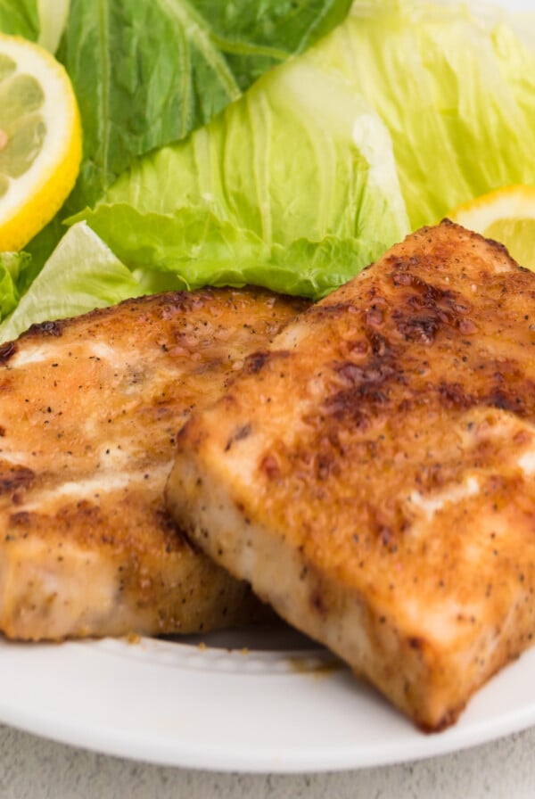 fully cooked air fryer frozen salmon on a white plate with a side salad and a lemon slice.