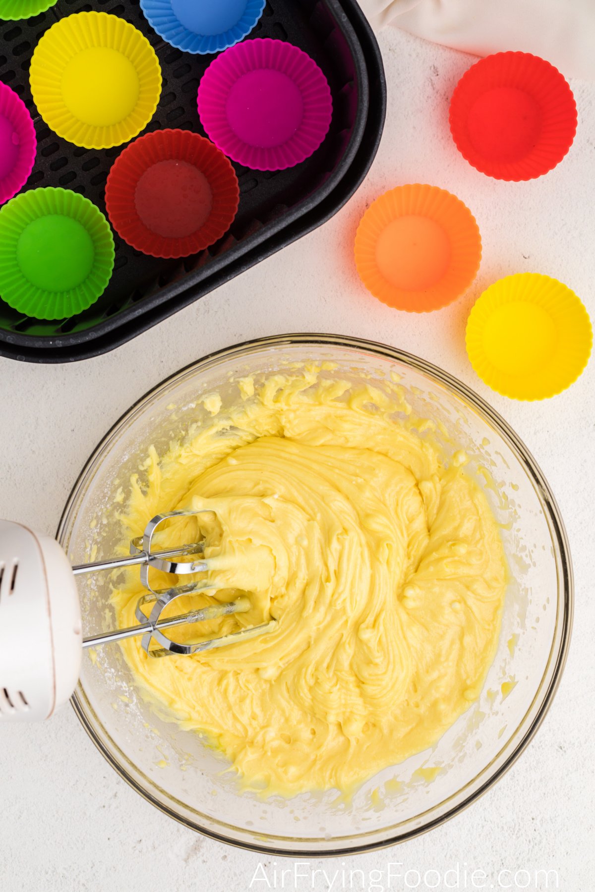 Ingredients mixed in a mixing bowl with a hand mixer and air fryer basket with silicone cups.
