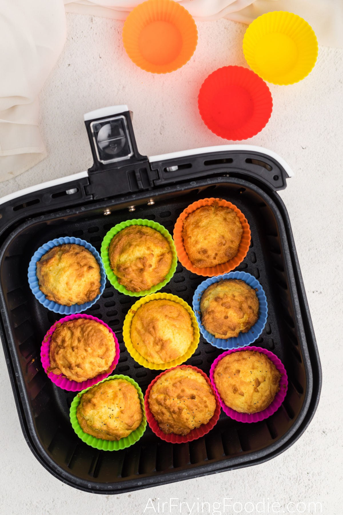 Golden brown air fried lemon poppy seed muffins in silicone muffin cups in the basket of the air fryer.