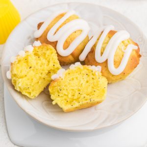 Lemon poppy seed muffins topped with lemon glaze, on a plate, with one muffin sliced in half.
