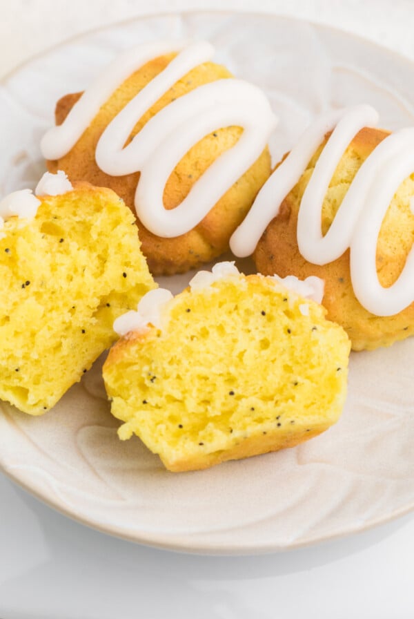 Air fryer lemon poppy seed muffins on a plate, topped with lemon glaze, with one muffin sliced in half.