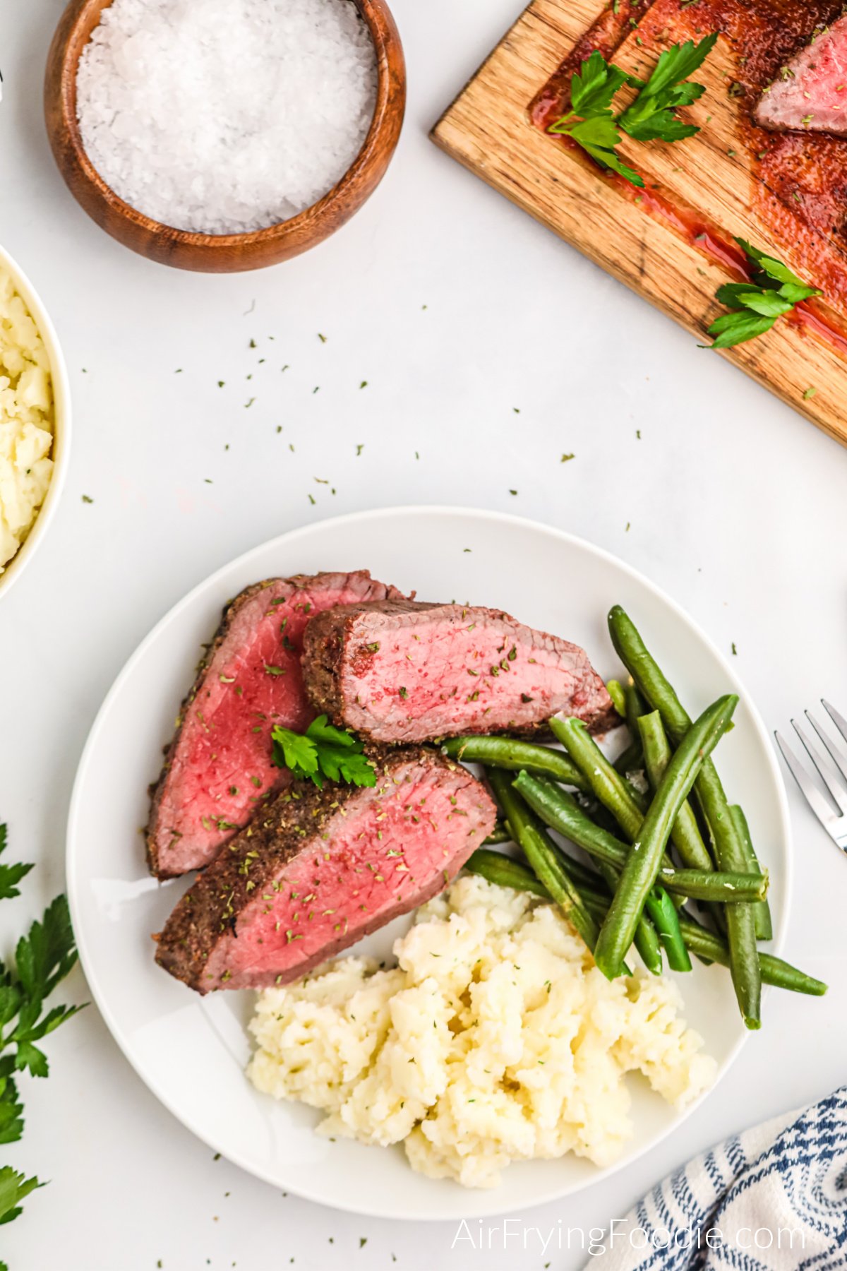 Seasoned London Broil made in the air fryer, served on a white plate with green beans and mashed potatoes.