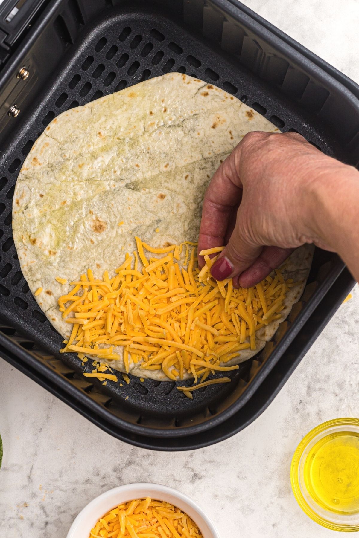 Sprinkling tortillas with cheddar cheese in the air fryer basket