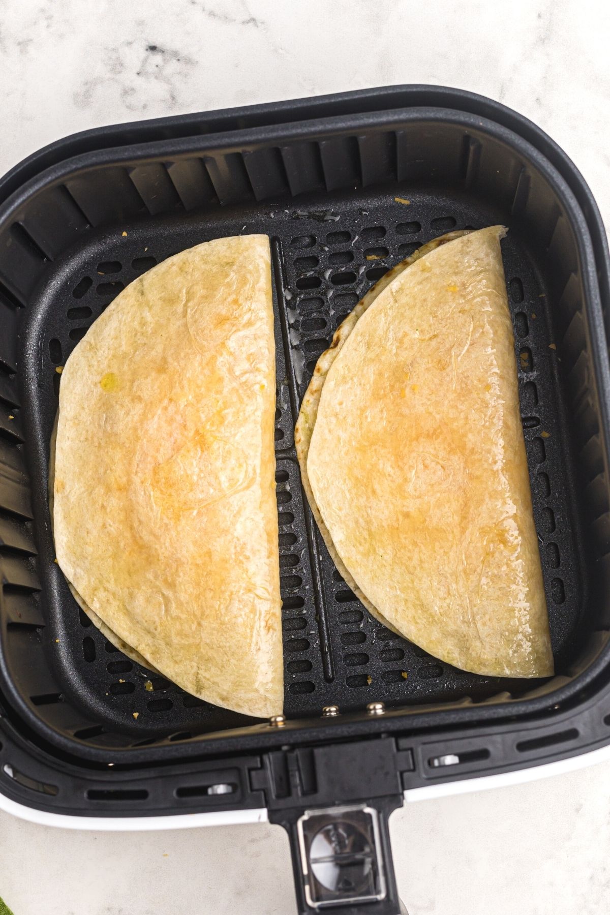 Uncooked tortillas filled with cheese in the air fryer basket.