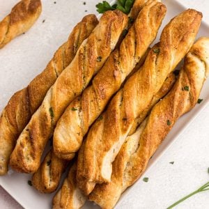 Golden breadsticks on a white plate garnished with parsley