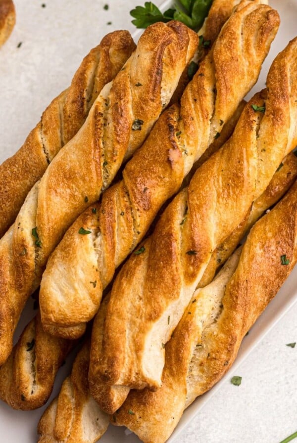 Golden breadsticks on a white plate garnished with parsley