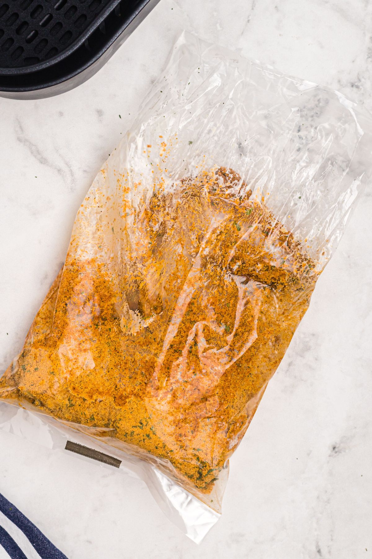 Plastic bag with chicken and seasonings shaken to coat chicken