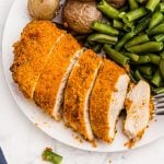 Golden crispy chicken sliced and served on a white plate with vegetables and a fork