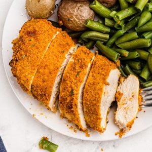 Golden crispy chicken sliced and served on a white plate with vegetables and a fork