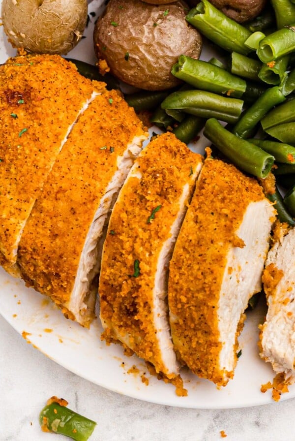 Golden crispy chicken sliced and served on a white plate with vegetables and a fork