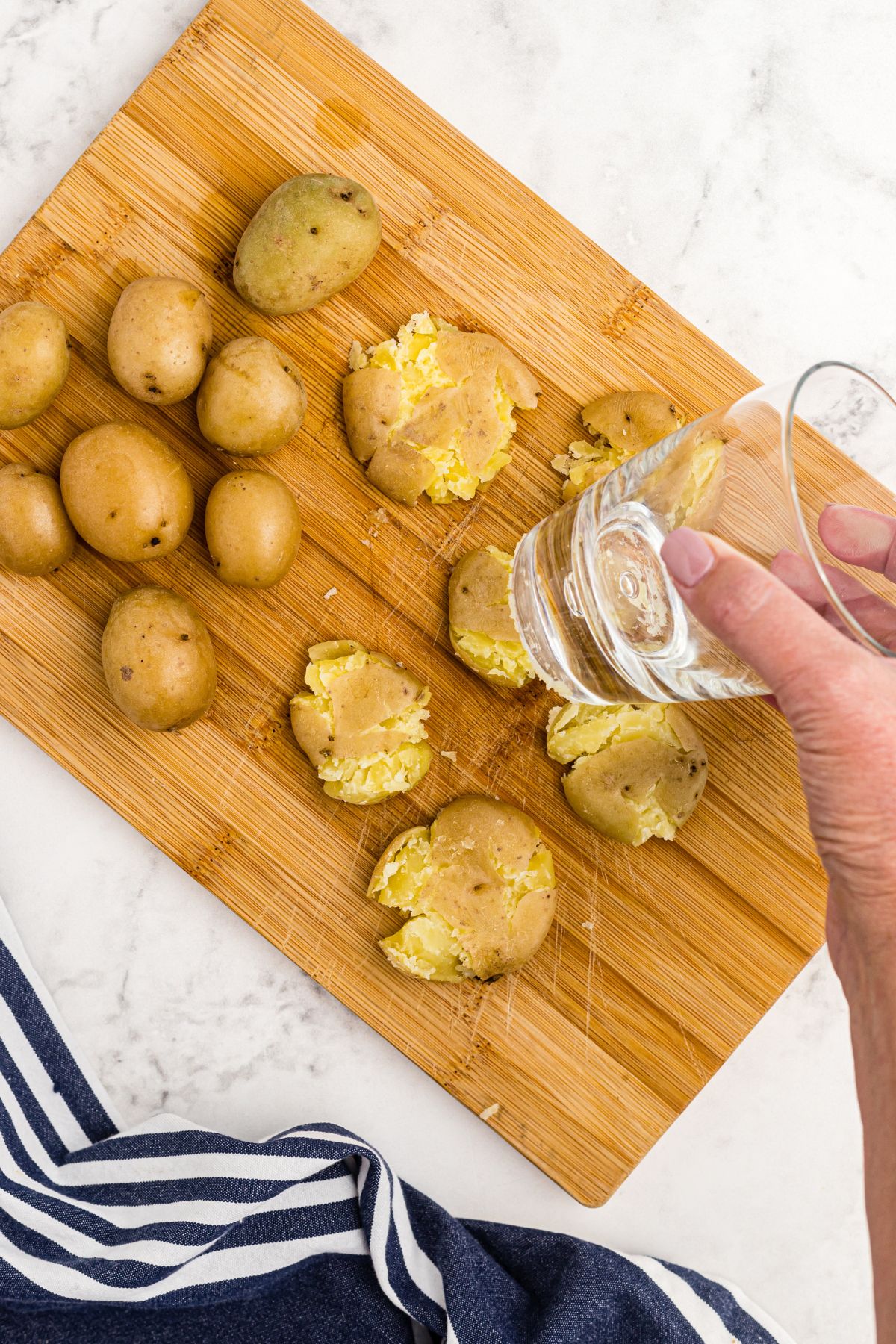 Soft golden potatoes on a wooden cutting board being smashed with a clear glass