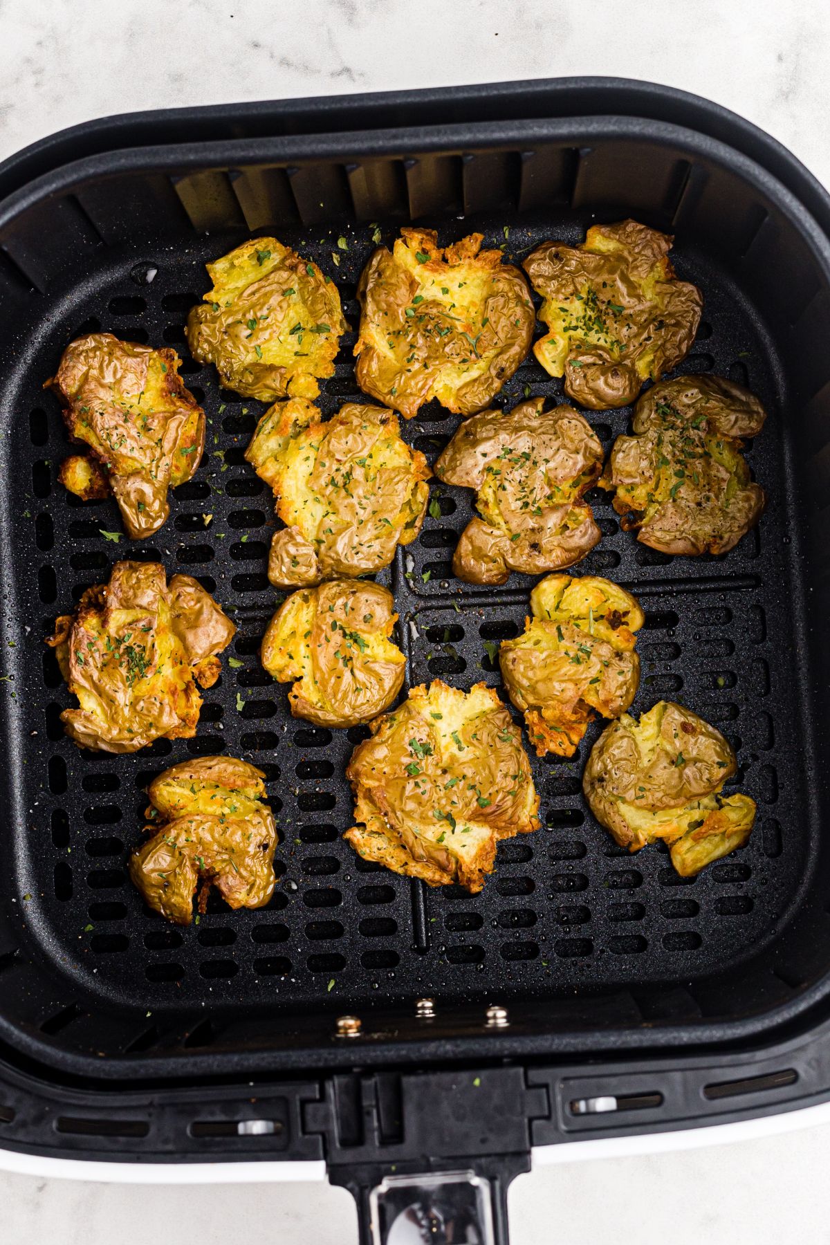 Golden crispy smashed potatoes in the air fryer basket after being cooked. 