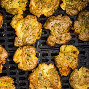 Golden crispy smashed potatoes in the air fryer basket after being cooked.