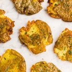 Golden crispy smashed potatoes on a white marble table garnished with parsley flakes