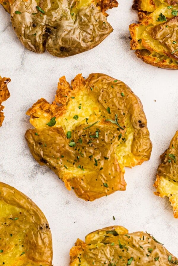 Golden crispy smashed potatoes on a white marble table garnished with parsley flakes