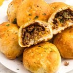 Golden biscuit dough filled with seasoned taco meat and cheddar cheese stacked on a white plate