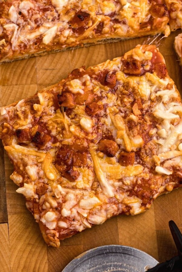 Cooked golden pizza ion a wooden cutting board with pizza cutter on table