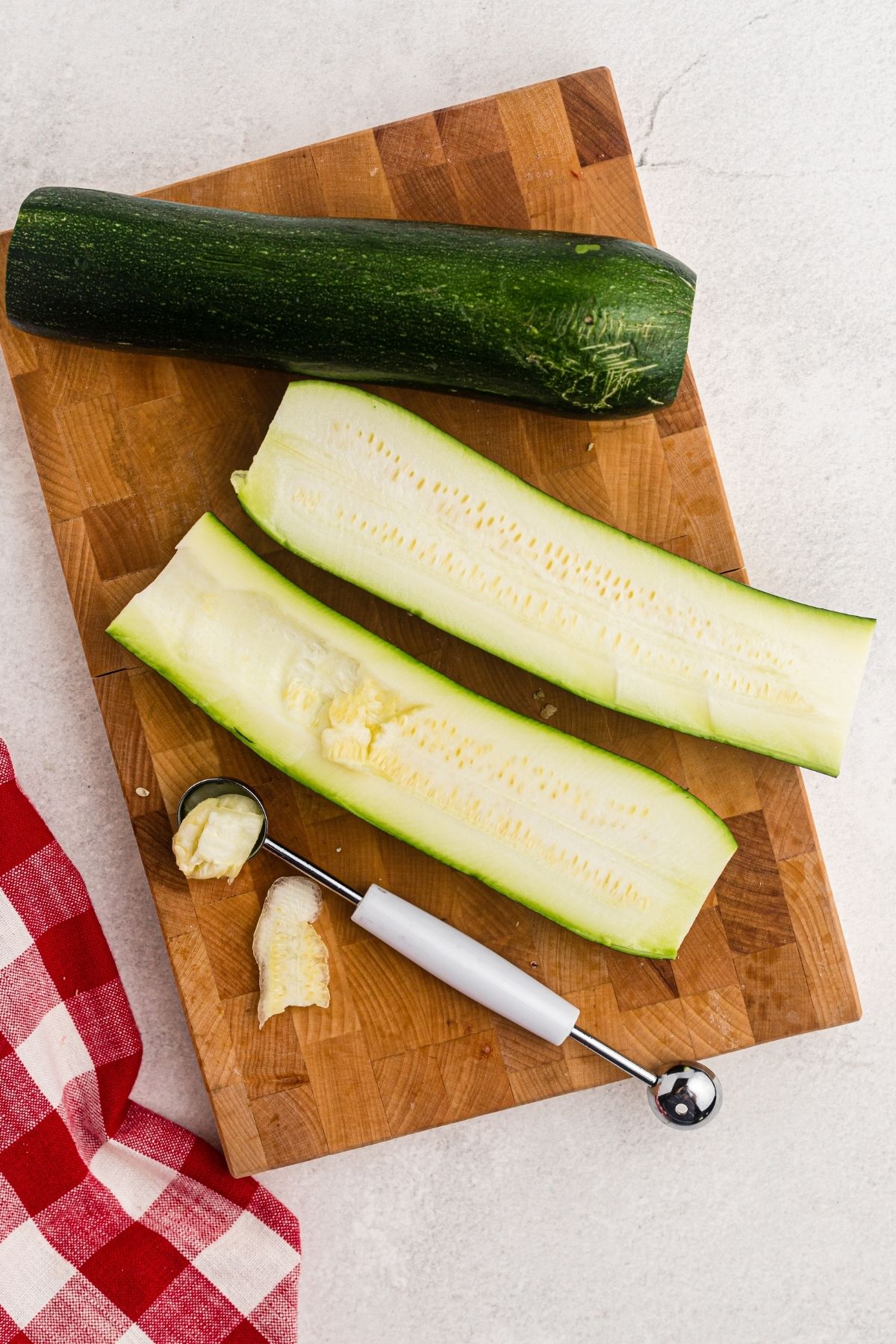 Zucchini sliced in half and then scooped out with melon baller on a cutting board