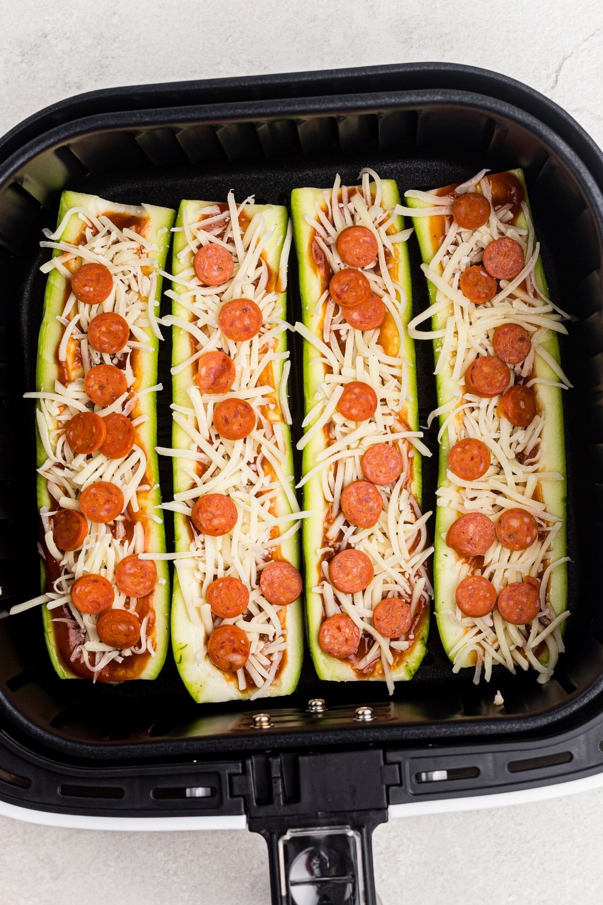Sliced zucchini topped with sauce, cheese, and pepperoni before being cooked in the air fryer basket