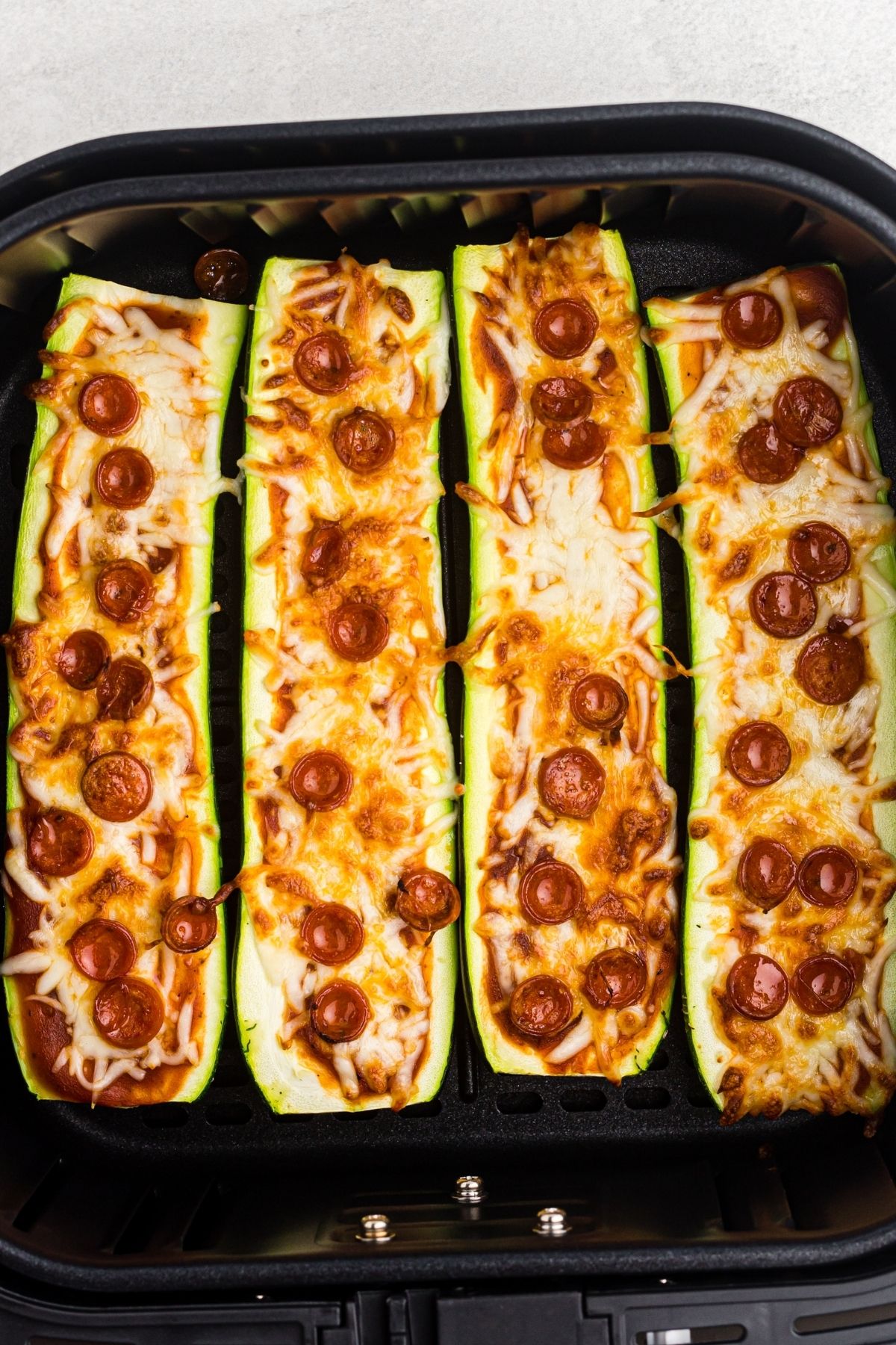 Zucchini pizza boats in the air fryer basket after being cooked until cheese is melted and zucchini is soft