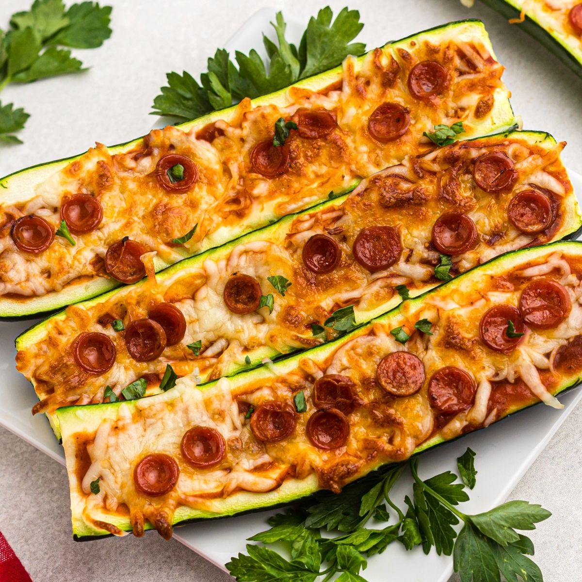 Golden cheesy zucchini boats on a white plate with parsley garnish