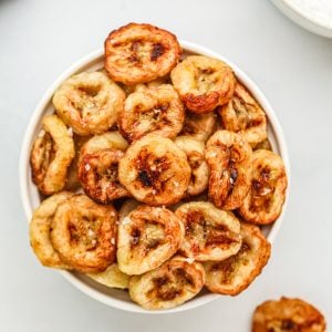 Banana chips made in the air fryer, served in a whote bowl with a sprinkling of kosher salt on top.