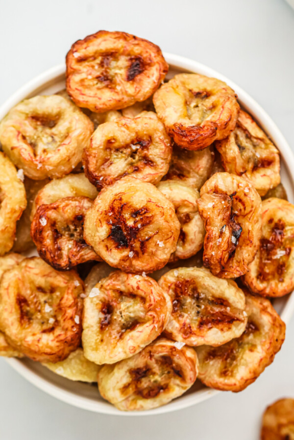 Banana chips made in the air fryer, served in a whote bowl with a sprinkling of kosher salt on top.