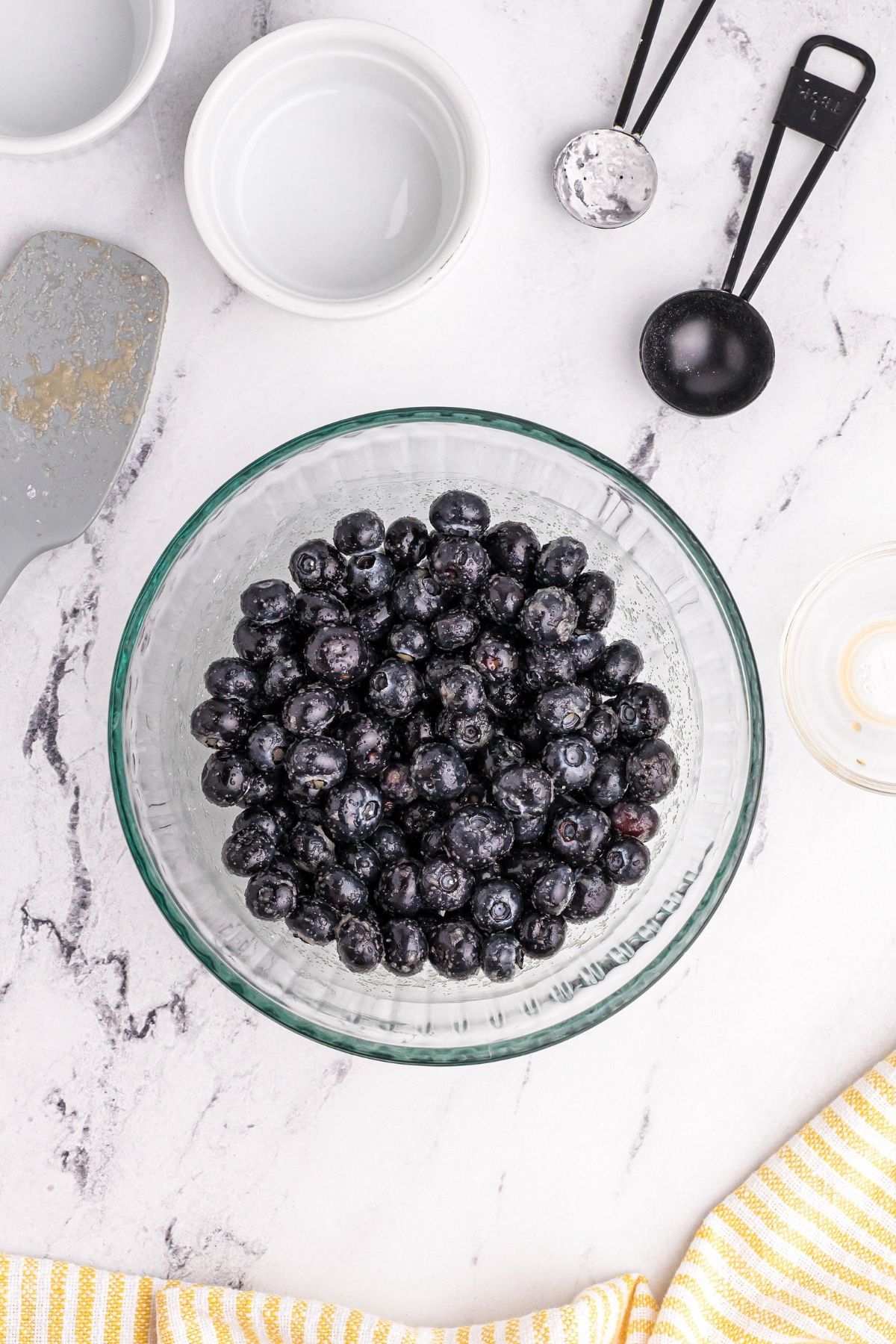 Clear bowl of blueberries with measuring spoons and bowls on the table