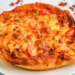 Breakfast pizza on a white plate ready to slice and serve.