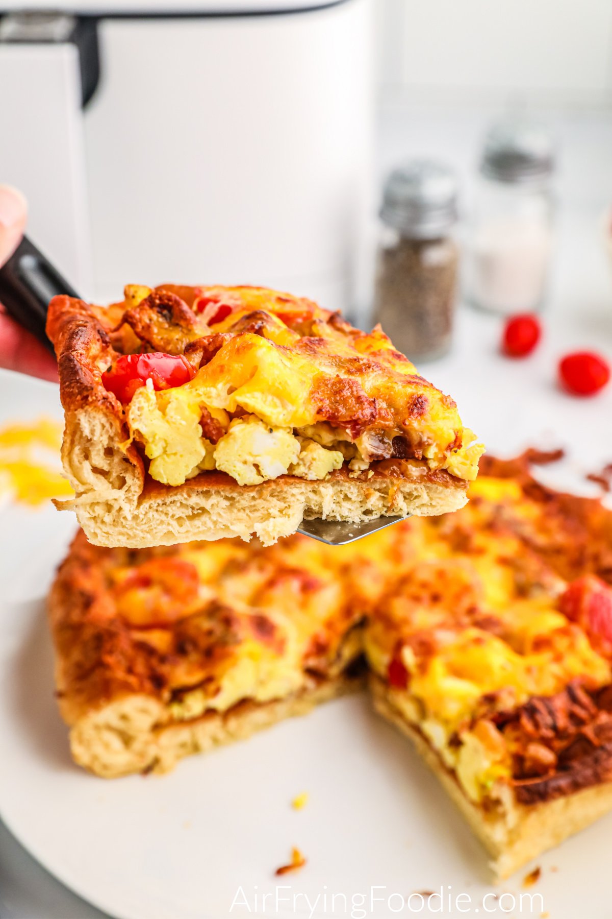 Slice of breakfast pizza made in the air fryer on a spatula.
