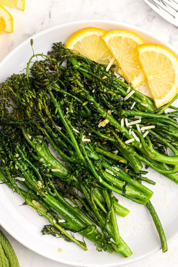 Juicy green broccolini florets on a white plate with lemon wedges