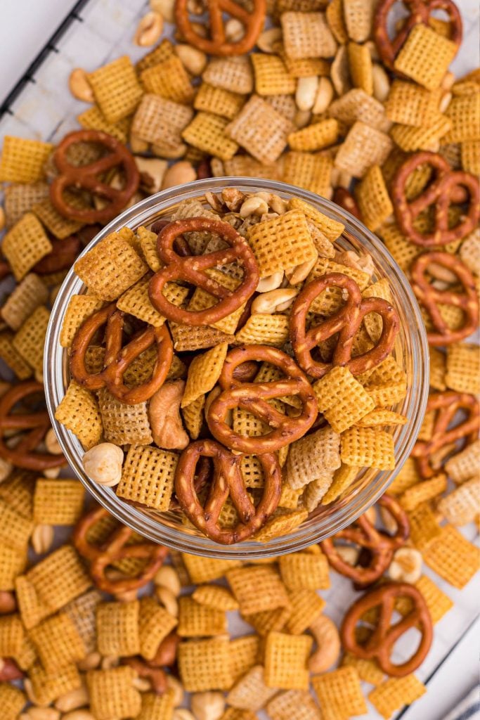 Clear glass bowl filled with Chex mix and more mix scattered around the table. 